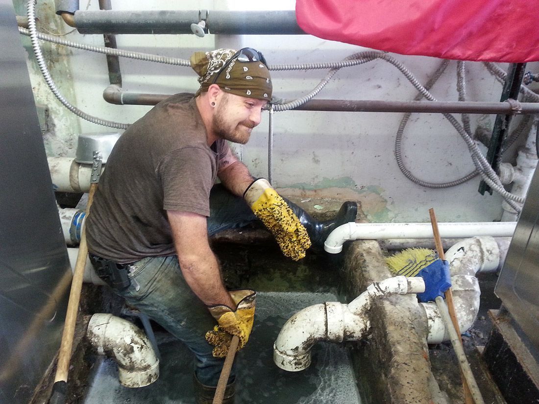 A man is kneeling down in a room with pipes.