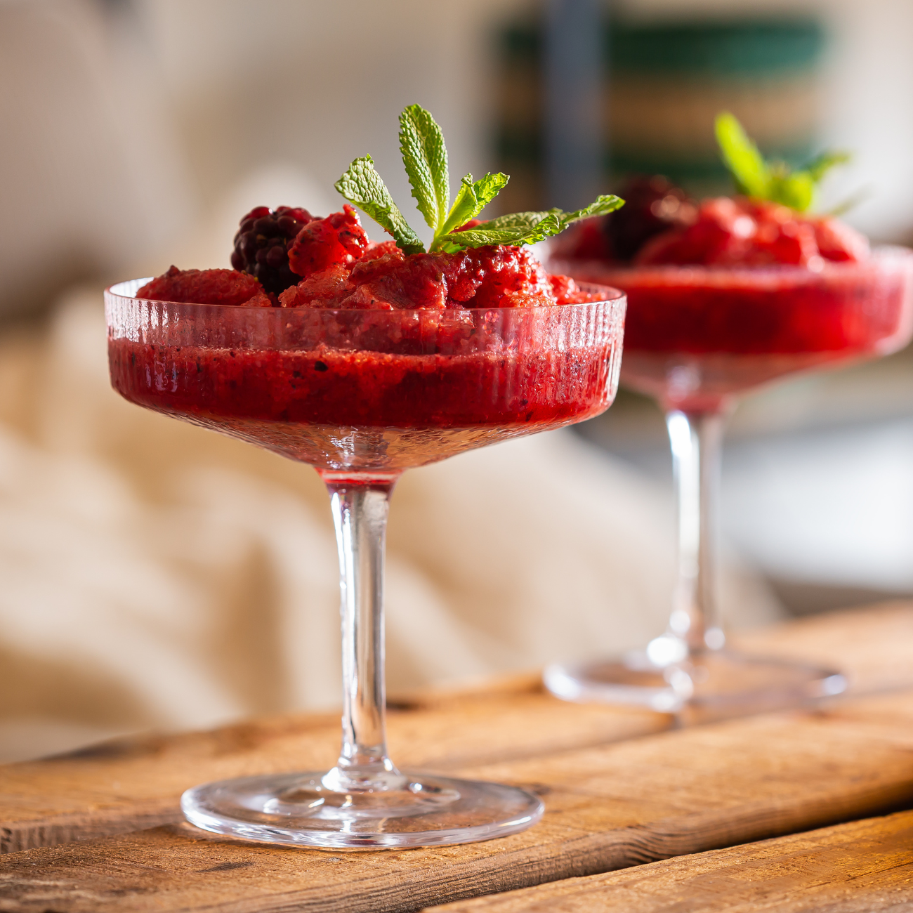 Two wine glasses filled with strawberry sauce and berries on a wooden table.