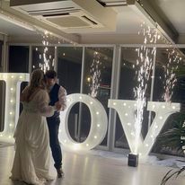 A bride and groom are dancing in front of a large love sign.