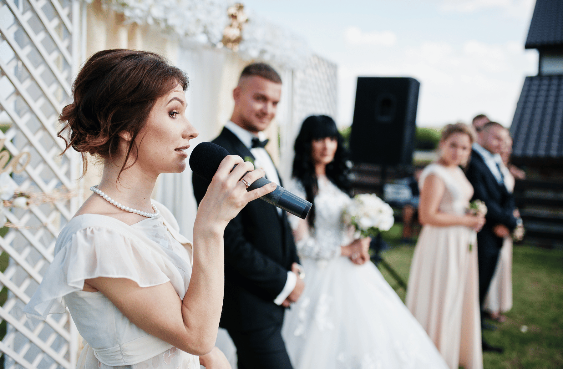 A woman is holding a microphone in front of a bride and groom at a wedding ceremony.