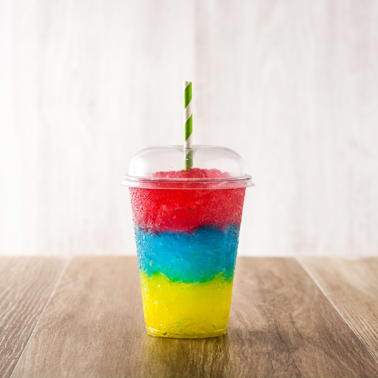 A cup of shaved ice with a straw on a wooden table.