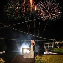 A bride and groom are kissing in front of a fireworks display.