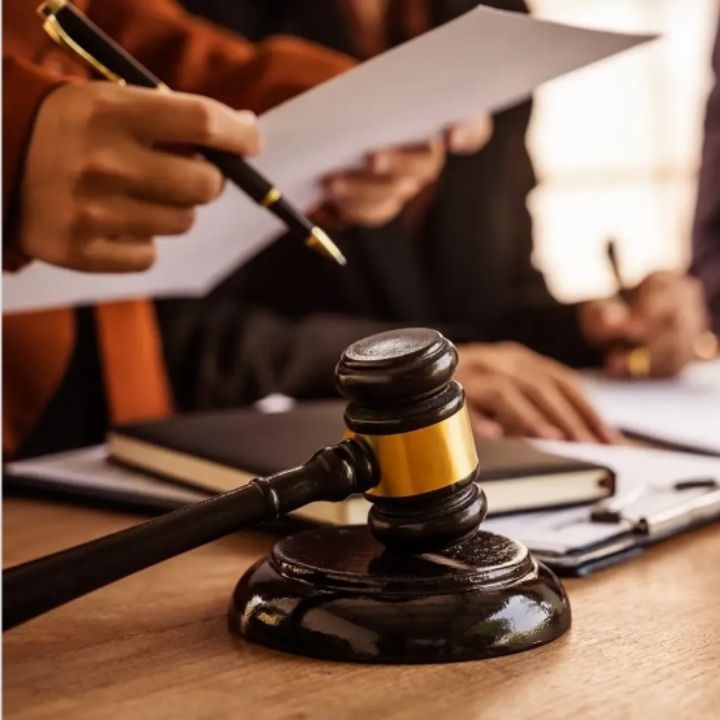 Gavel on a wooden desk, people reviewing documents in a legal setting.