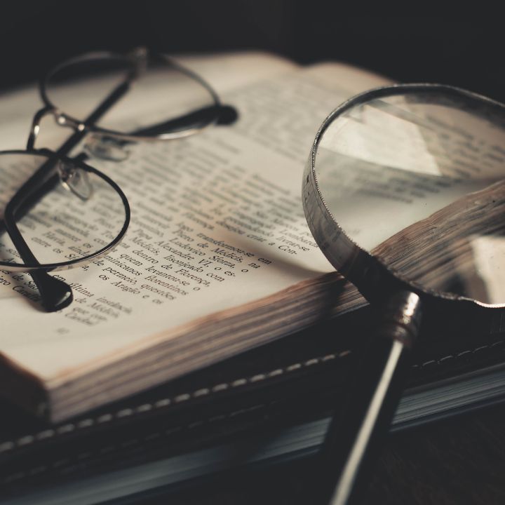Eyeglasses and magnifying glass on an open book, suggesting research or investigation. Private Investigator Services In Gallatin TN 