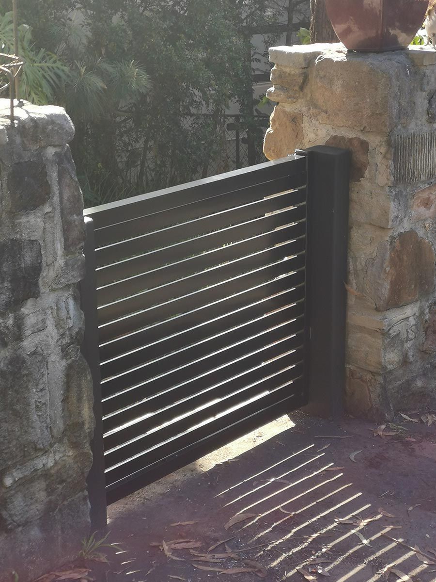 A Black Gate With a Stone Wall Behind It — WeFence in Lisarow, NSW