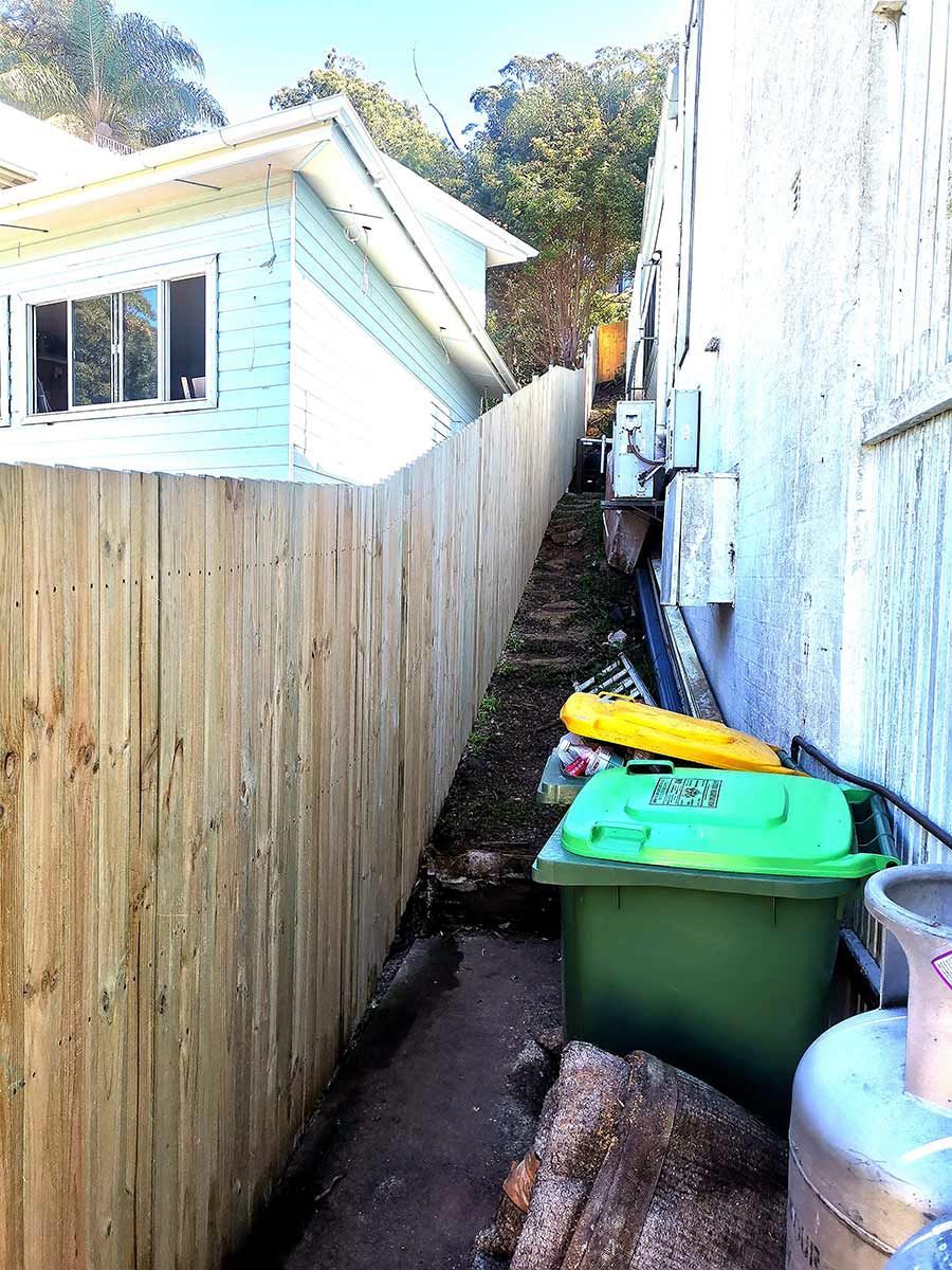 A Wooden Fence Along the Side of a House With Trash Cans — WeFence in Lisarow, NSW
