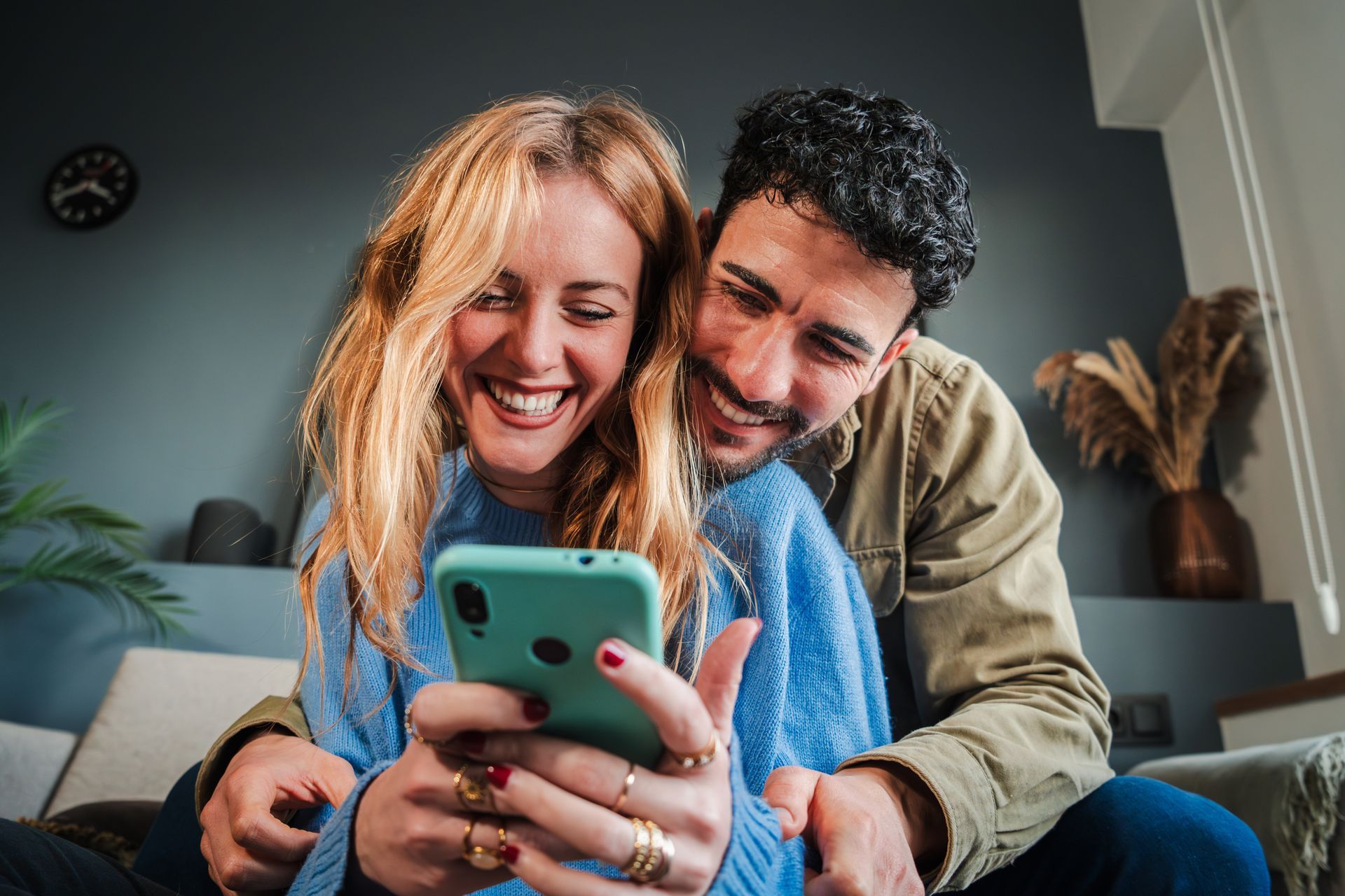 A man and a woman are sitting on a couch looking at a cell phone.