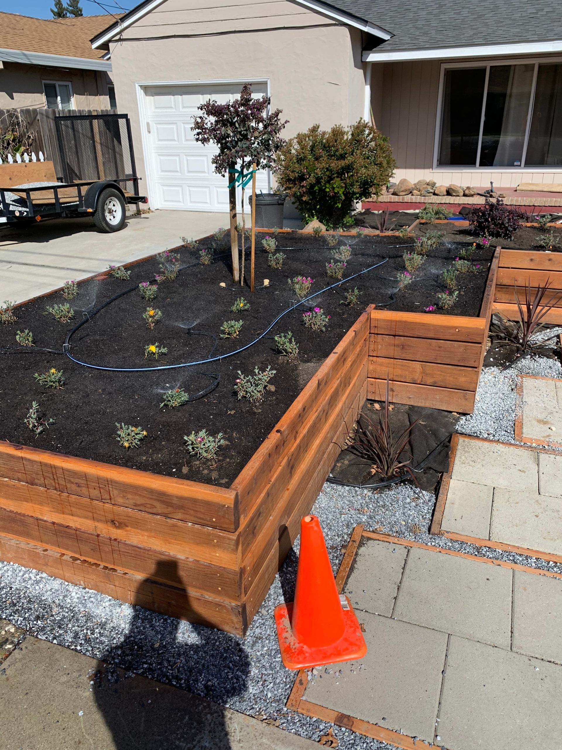 A wooden planter with plants in it is in front of a house.