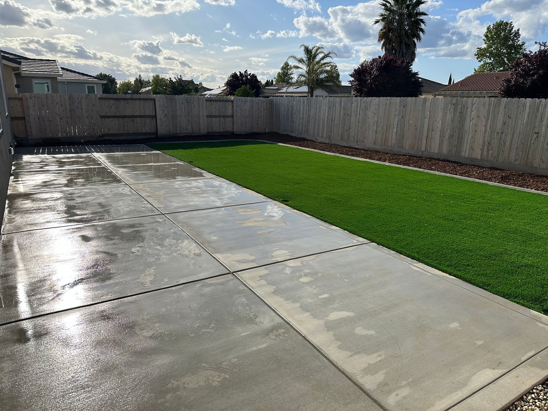 A backyard with a concrete driveway and a wooden fence