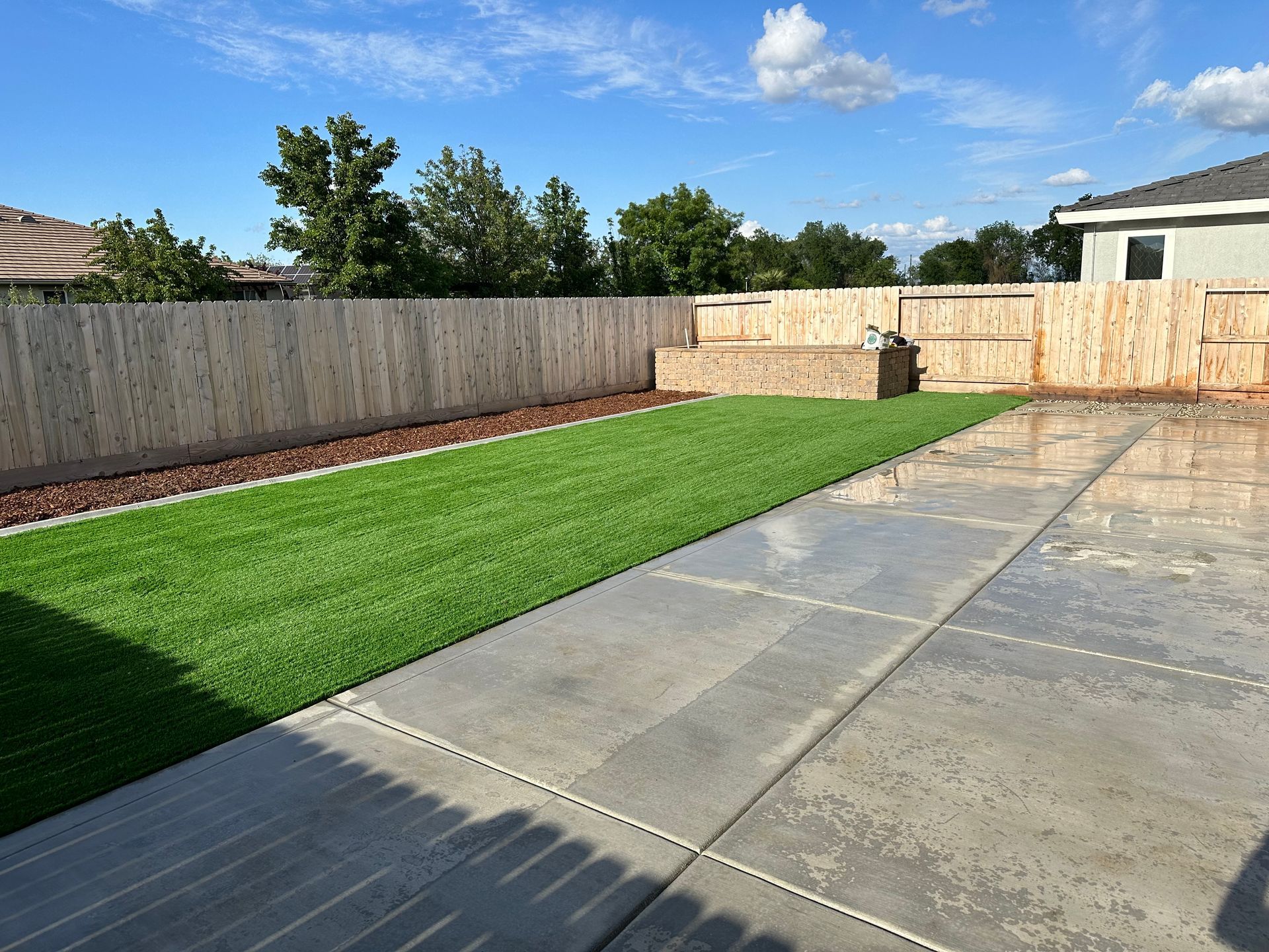A backyard with a wooden fence and a concrete walkway