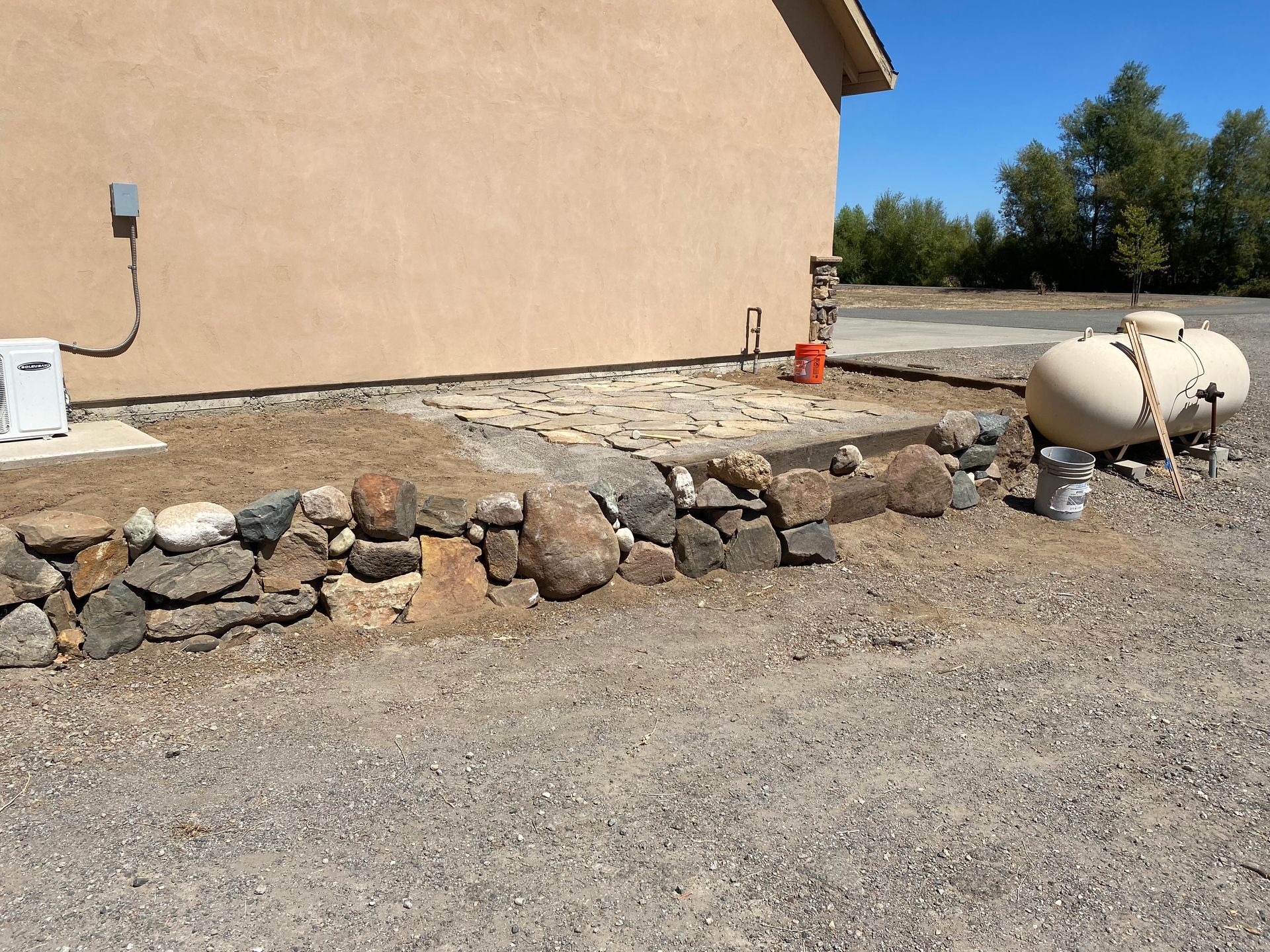 A propane tank is sitting next to a stone wall
