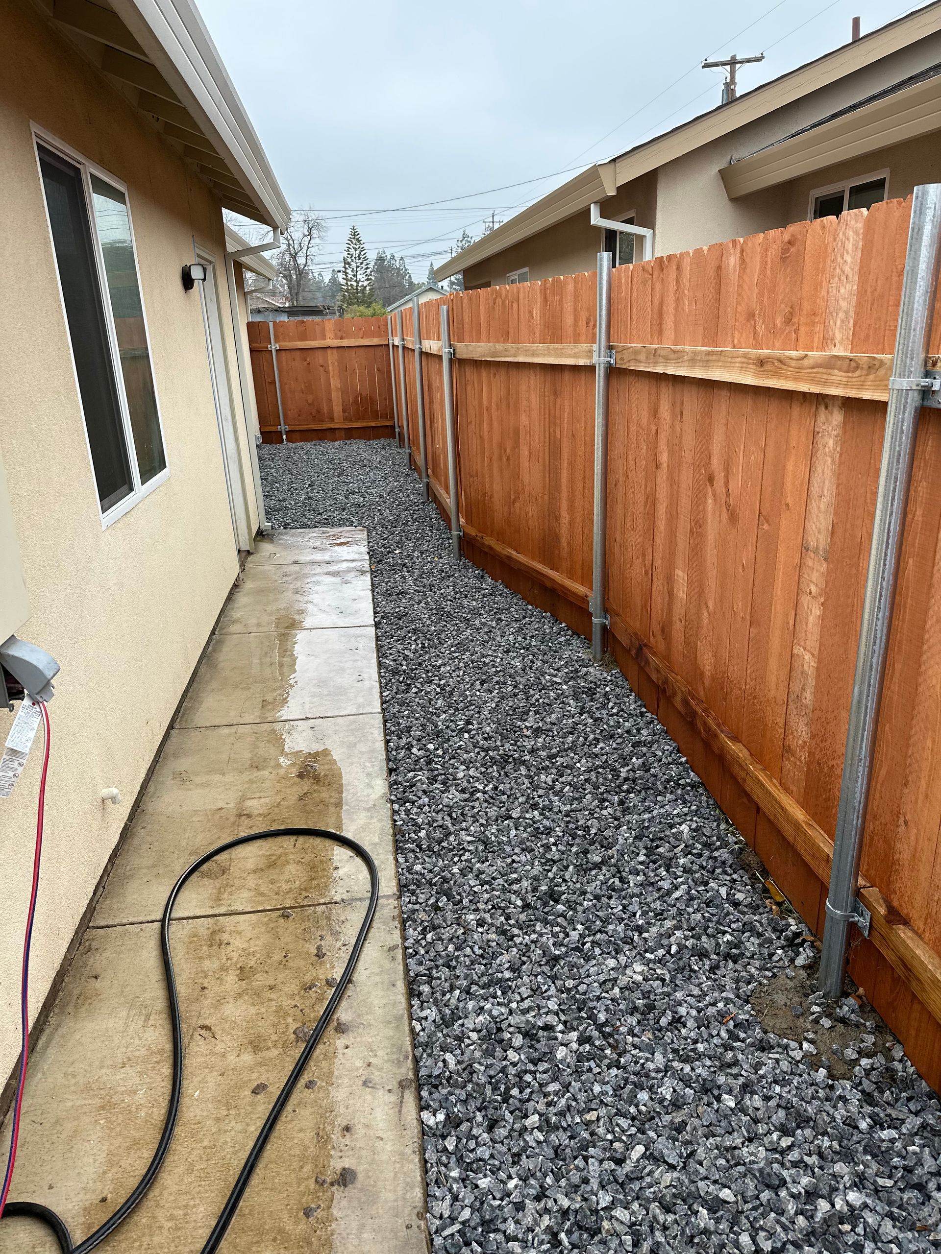 A wooden fence surrounds a gravel area next to a house.