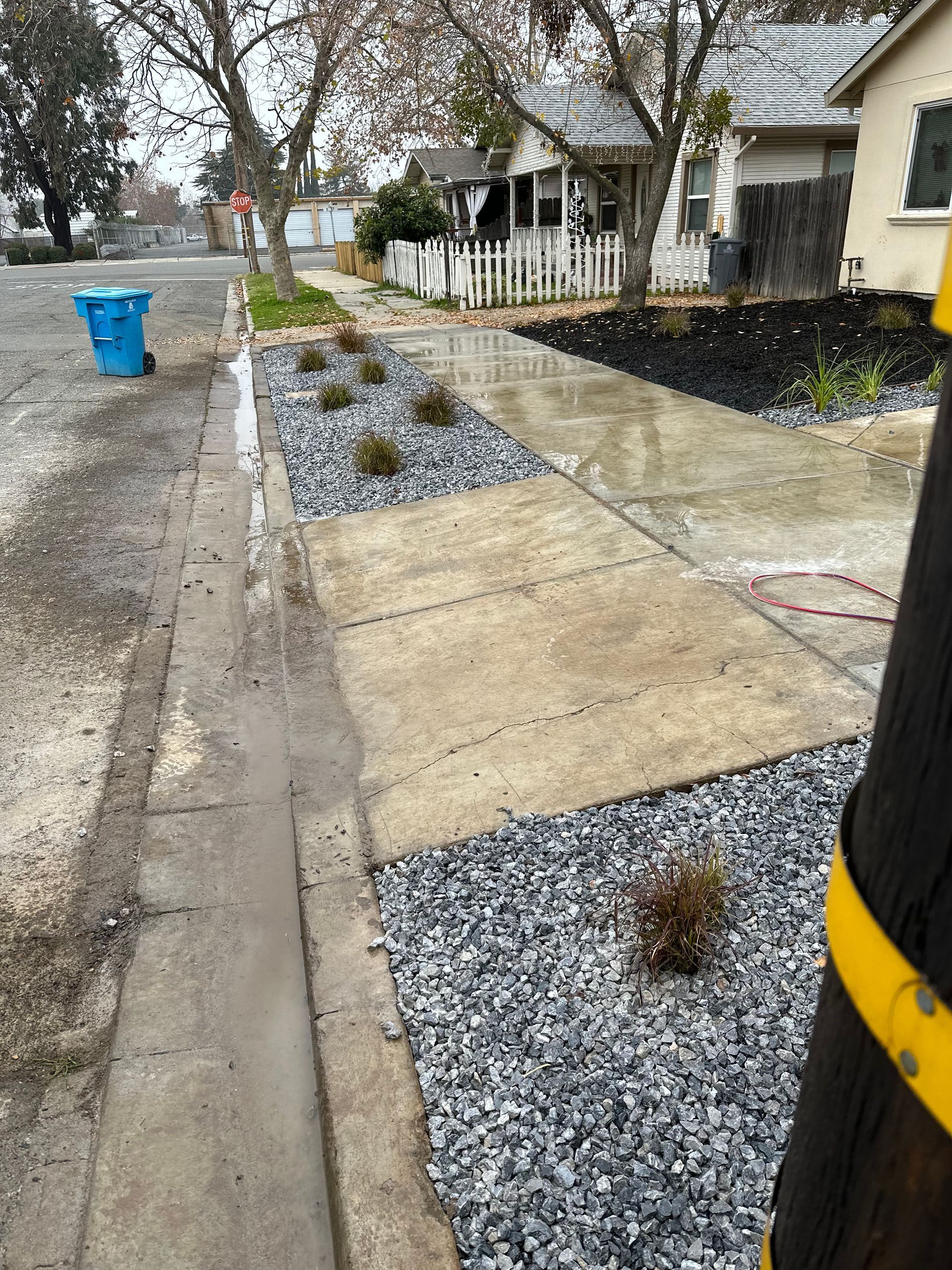 A sidewalk with a blue trash can on the side of it.