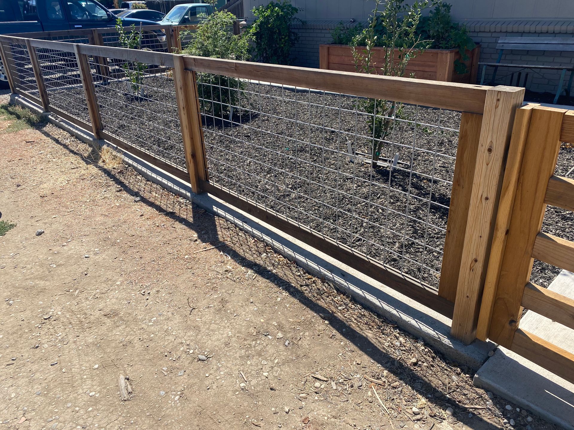 A wooden fence with a chain link fence surrounding a gravel area.