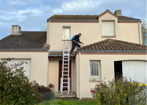 A person in dark clothing climbs a ladder placed on a house porch to access the roof.
