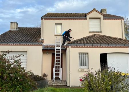 Two workers in hard hats install a metal snow guard on a black standing-seam roof.