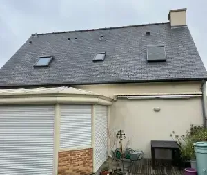 A slate roof house with three skylights, an attached sunroom with white rolling shutters, and a patio area.