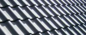 A close-up, angled view of dark grey, overlapping S-shaped roof tiles with strong sunlight and shadows.
