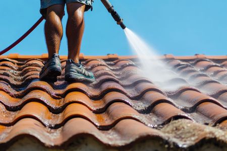 A person in a green shirt and work gloves applies black waterproofing membrane to a wall on a rooftop.