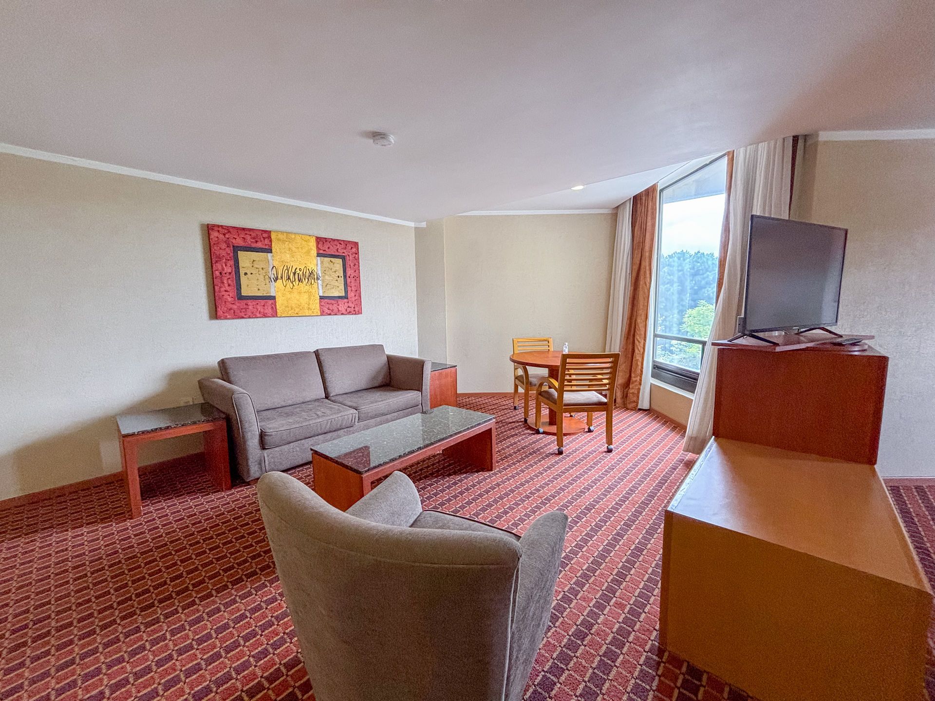 Una sala de estar de una suite de hotel con un sofá gris, un sillón, una mesa de centro.