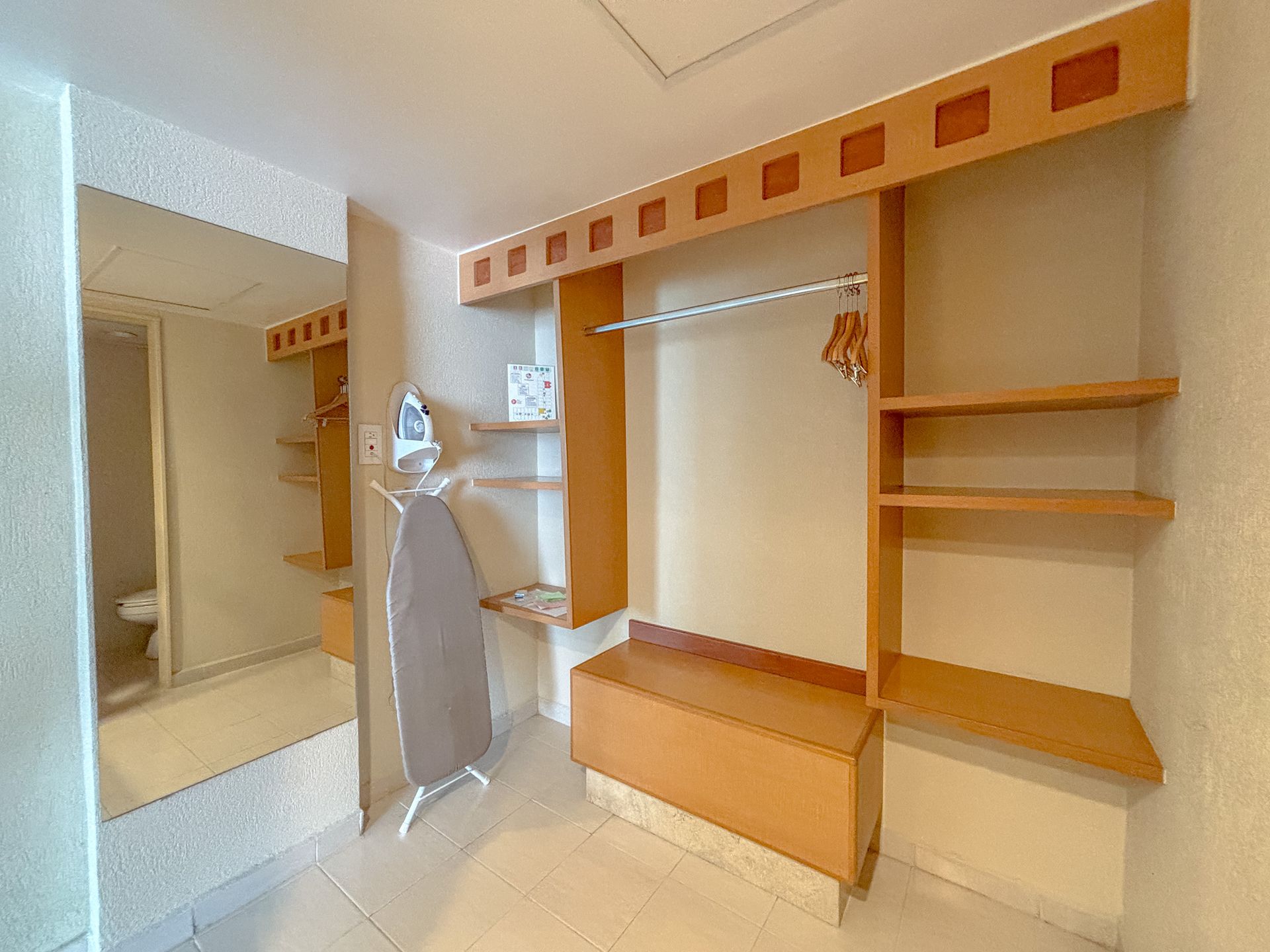 Un armario abierto con estantes de madera clara, una barra para colgar ropa