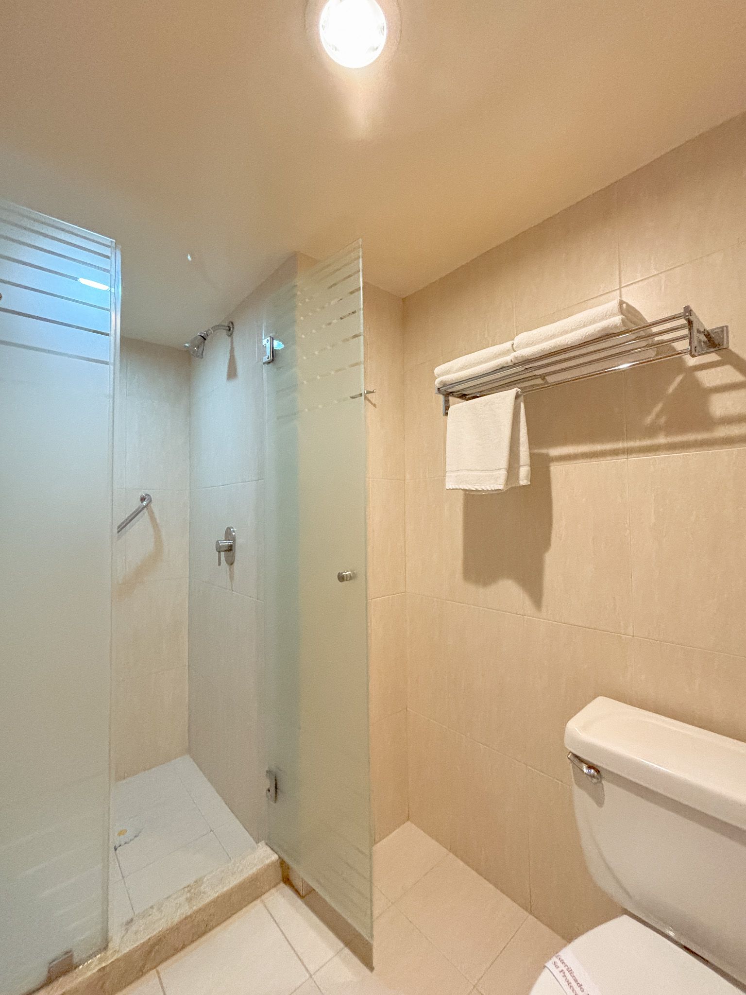 Un moderno baño de hotel con ducha acristalada, toallero de pared con toallas blancas limpias y un inodoro.