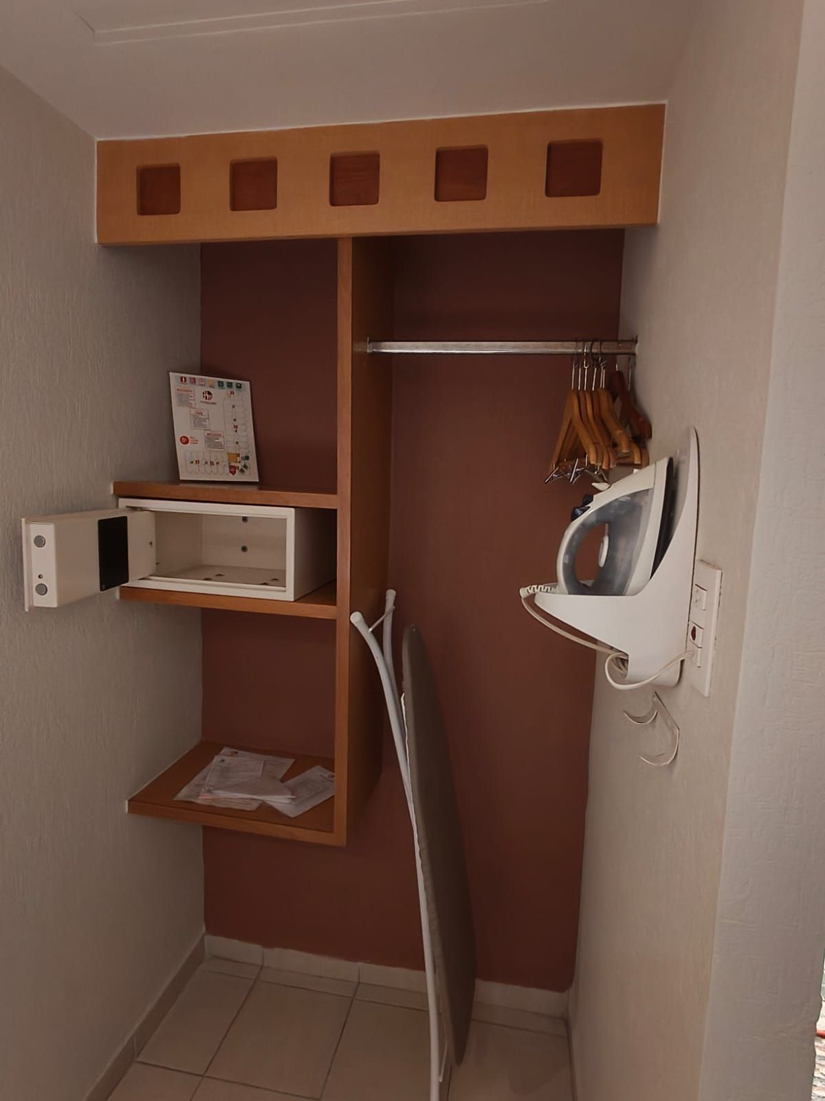 Un armario de hotel con caja fuerte, estantes de madera, una barra para colgar ropa con perchas