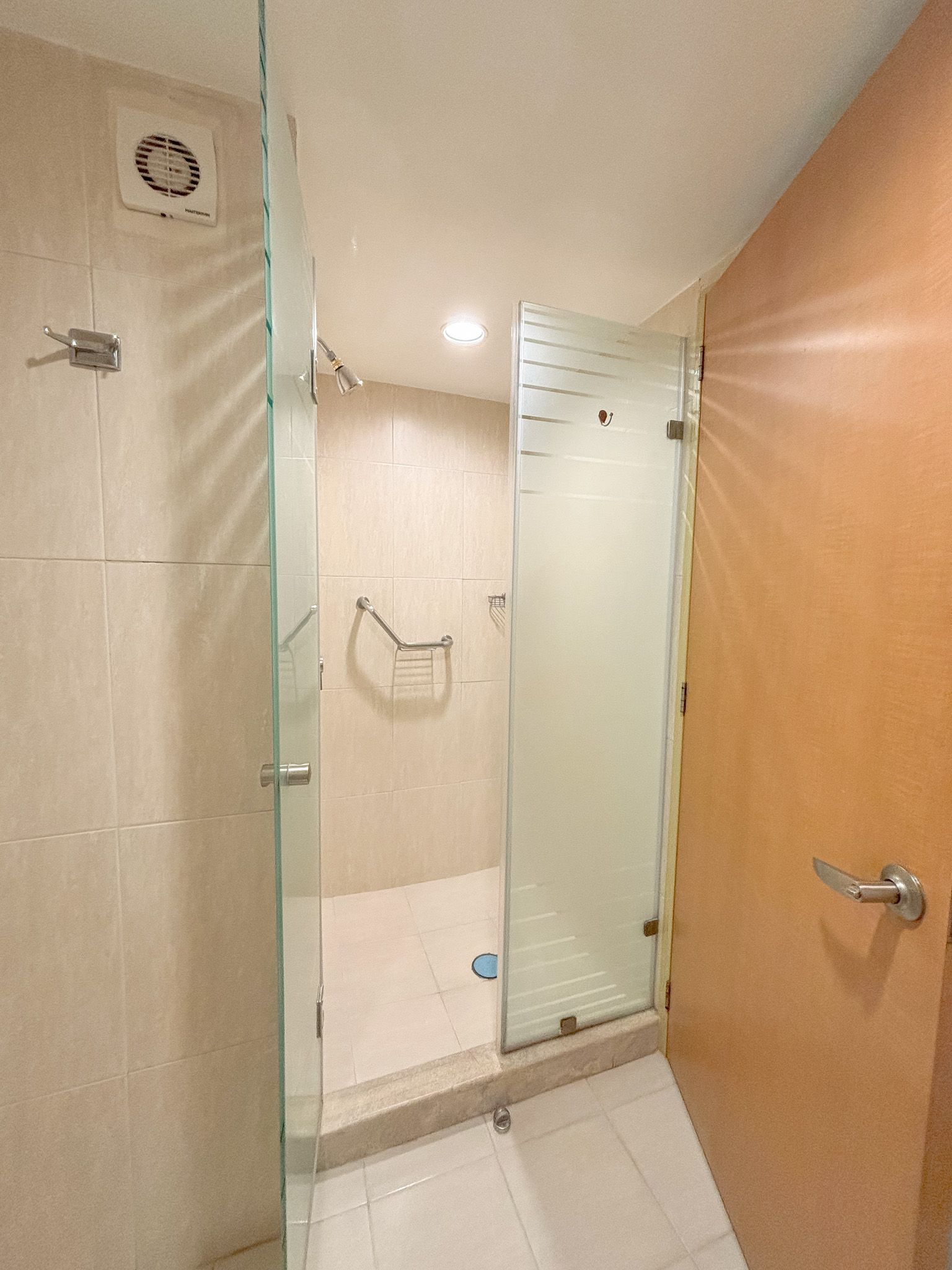 Una cabina de ducha con azulejos beige y barra de apoyo