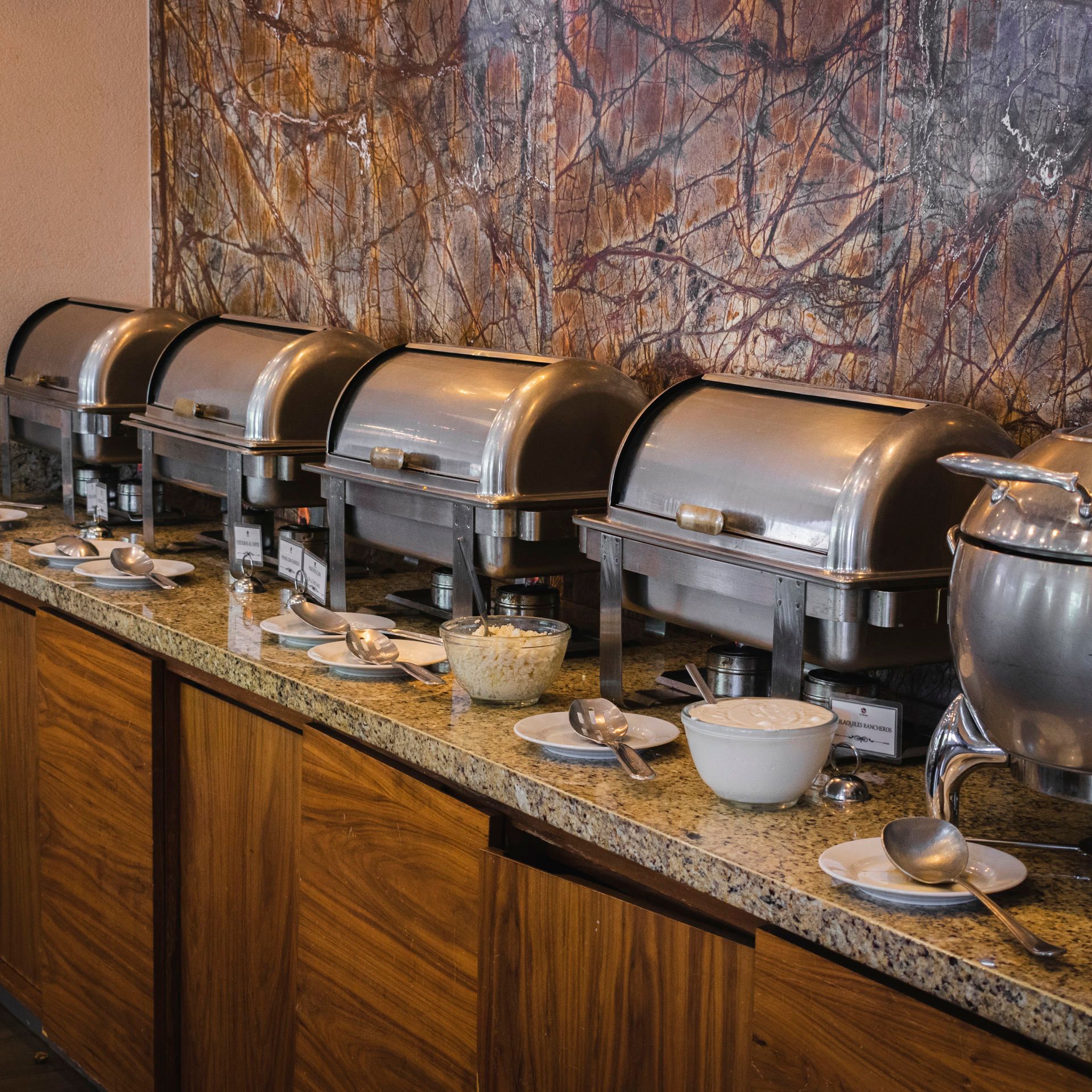 Un bufé con varios recipientes de plata para mantener la comida caliente 