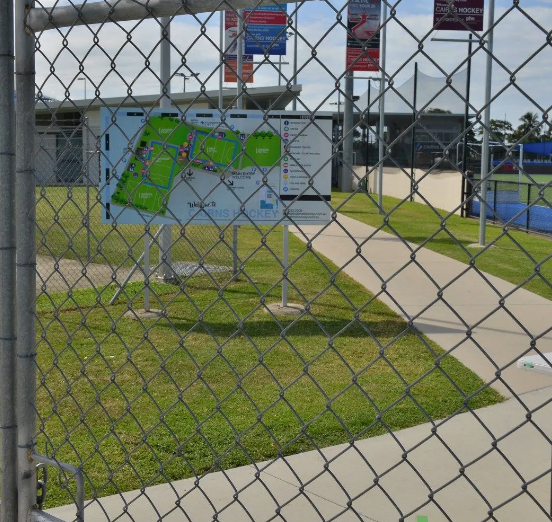 Chain link fence with a map of playing fields, green grass, and a pathway.