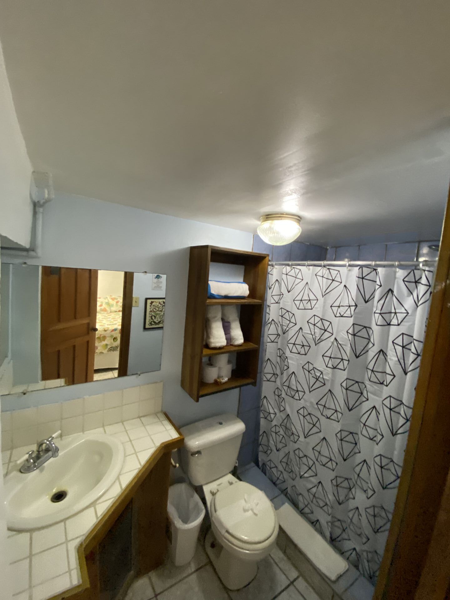 Bathroom with sink, toilet, and shower with geometric curtain; blue walls, wooden accents.