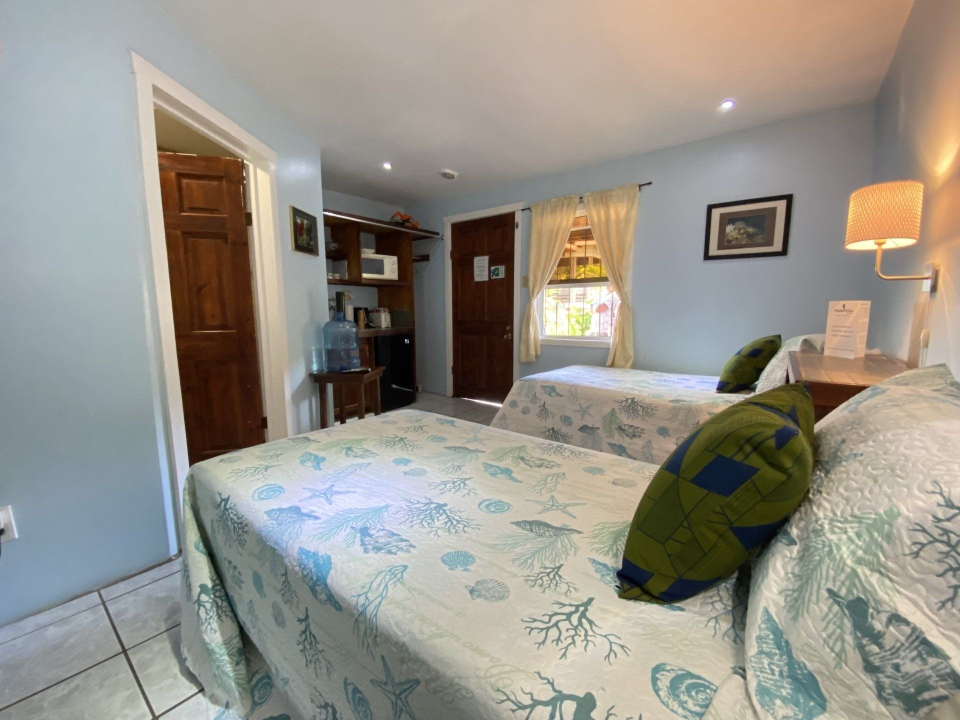 A hotel room with two twin beds, light blue walls, and a door to a bathroom.