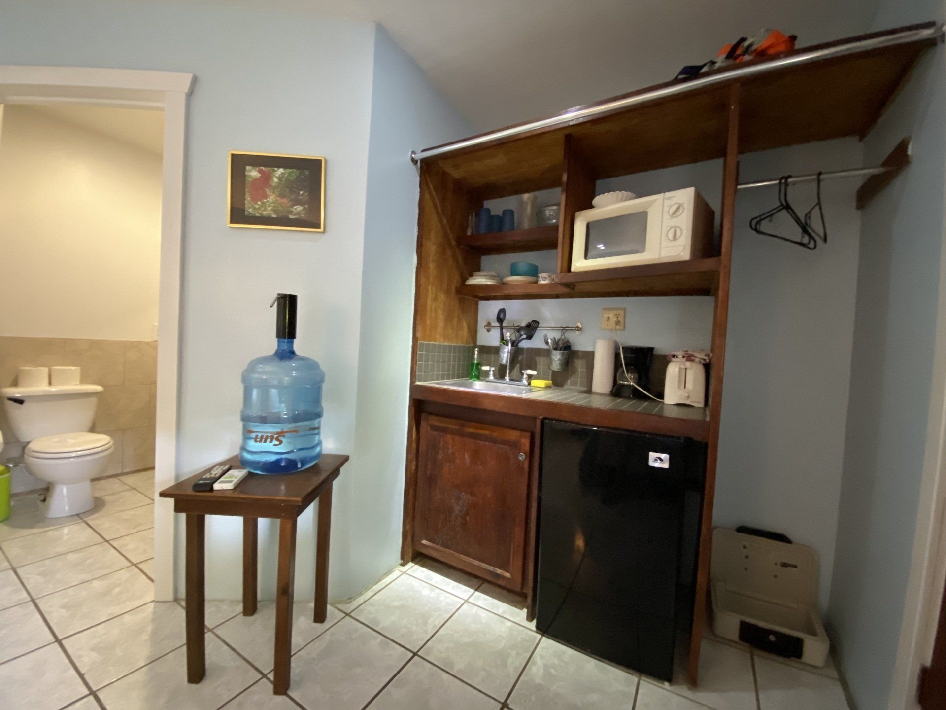 A small kitchenette with a microwave, mini-fridge, and sink. A large water jug sits on a table.