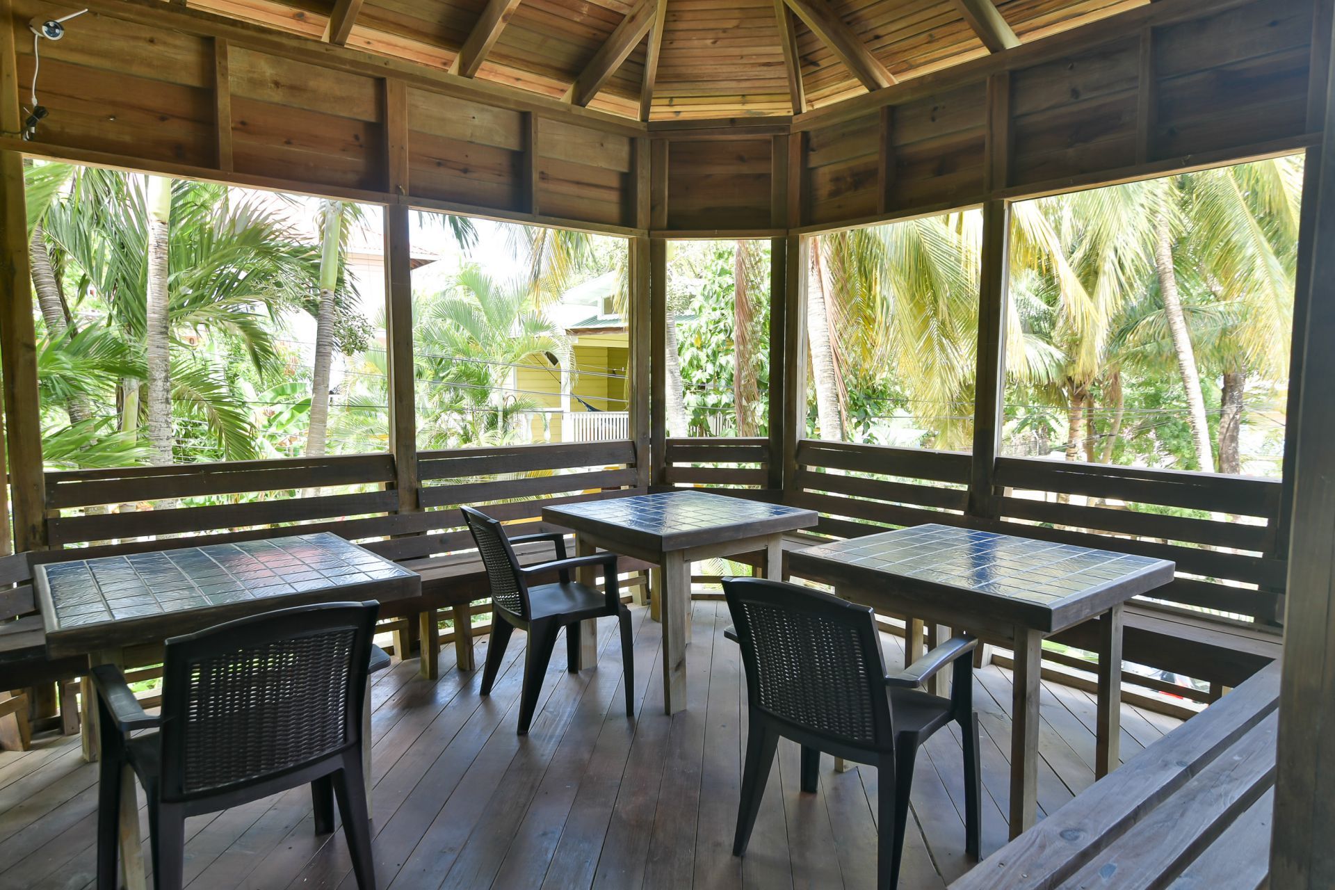 Wooden gazebo with tables and chairs overlooking lush green foliage.