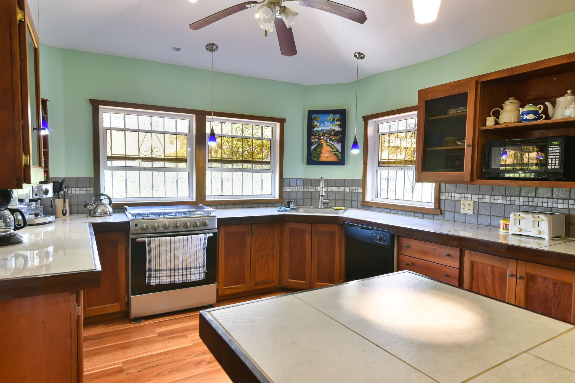 Kitchen with wooden cabinets, tile counters, and green walls. A stainless steel range and island are featured.