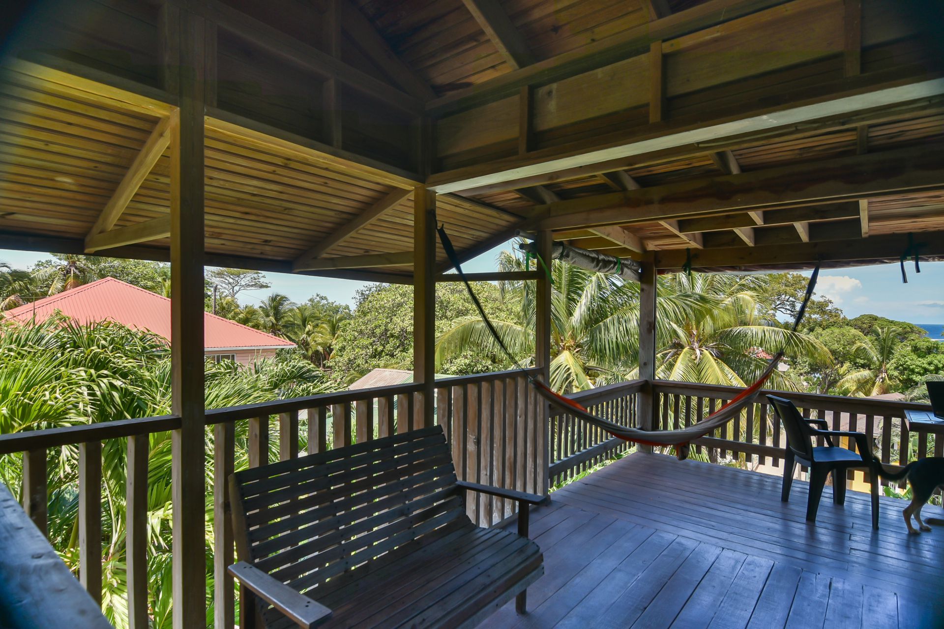 Wooden porch with bench, hammock, and chairs, overlooking lush trees and ocean.