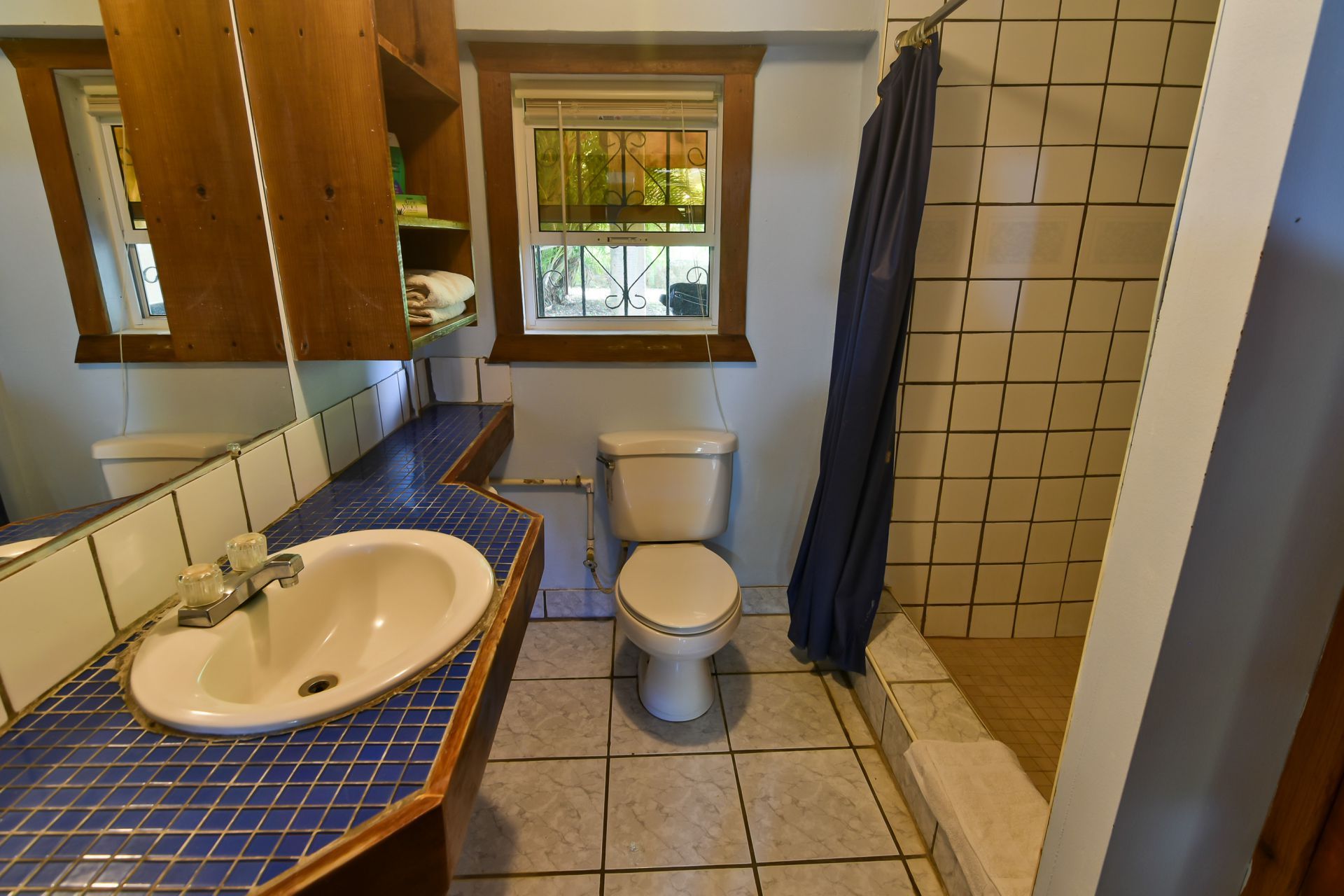 Bathroom with blue tiled countertop, white toilet, and shower behind a blue curtain.