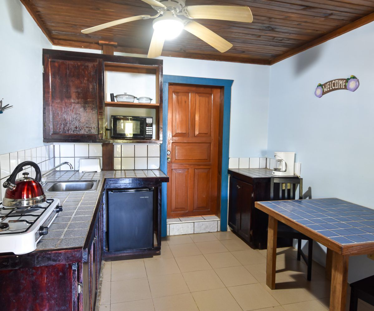 Small kitchen with brown cabinets, appliances, and a wooden door. A table and stove are in view.