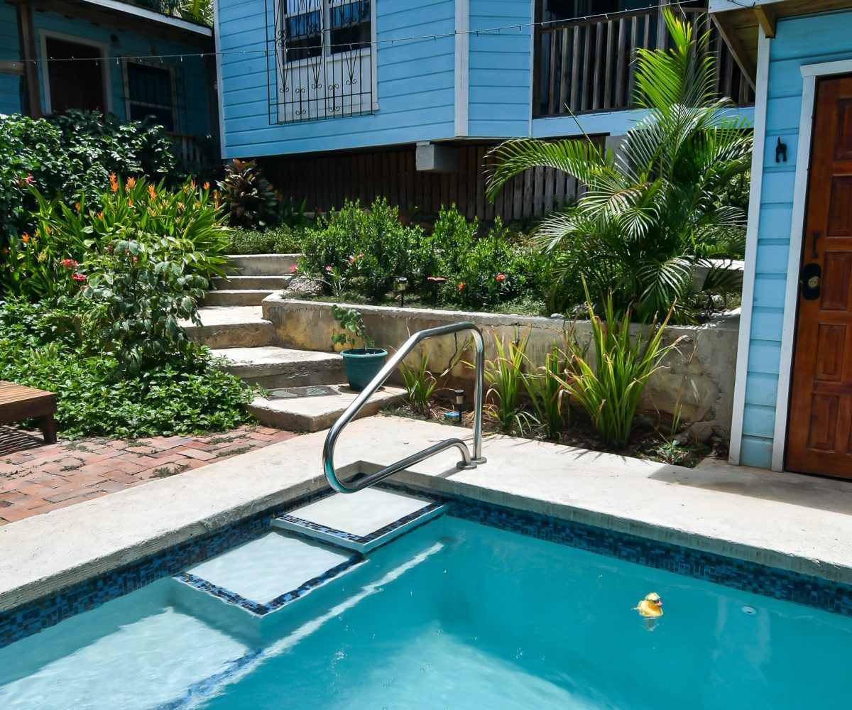 Swimming pool with steps and railing, beside a light blue house with steps up to the entrance.