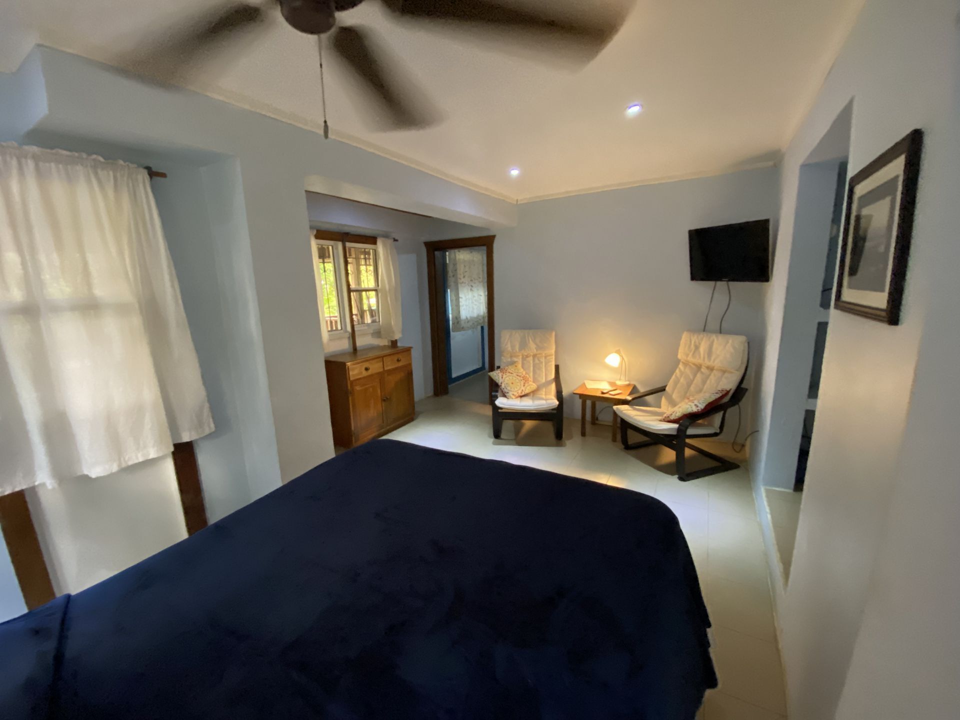 Bedroom with a bed, chairs, small TV, and a view of outside. Blue walls and white floors.