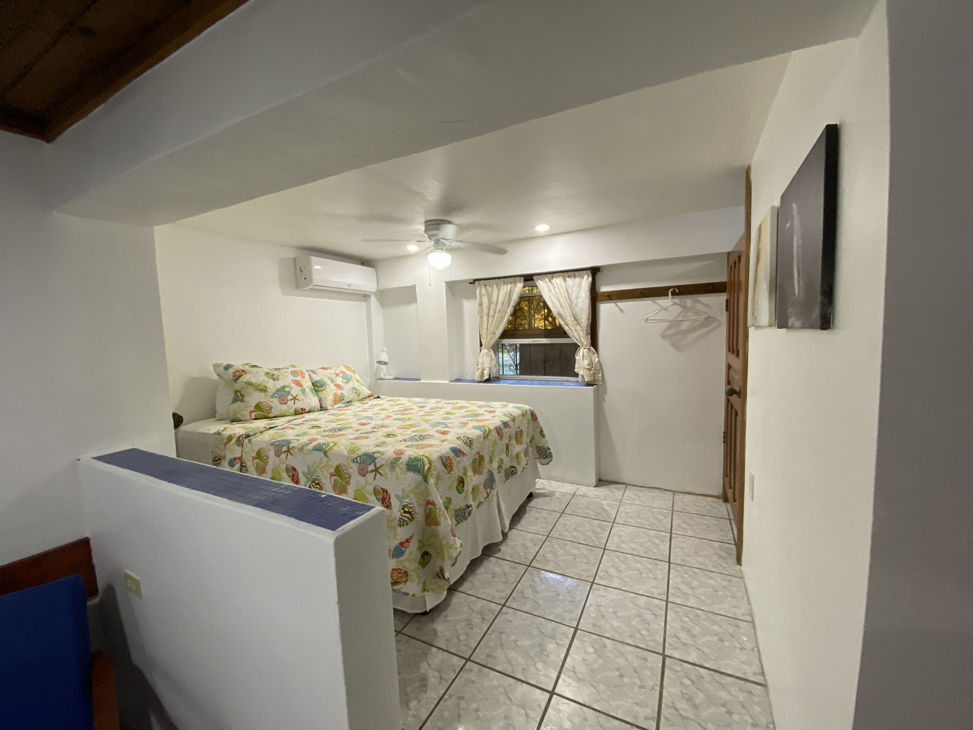 Small white bedroom with bed, window, and tiled floor.