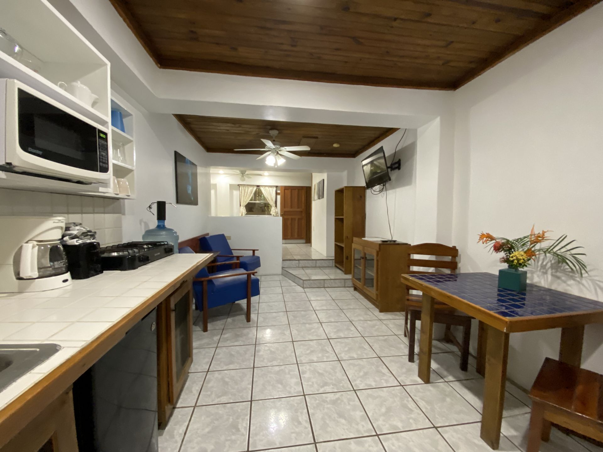 Interior view of a small apartment with kitchen, dining, and living areas; wood ceiling and tile floor.
