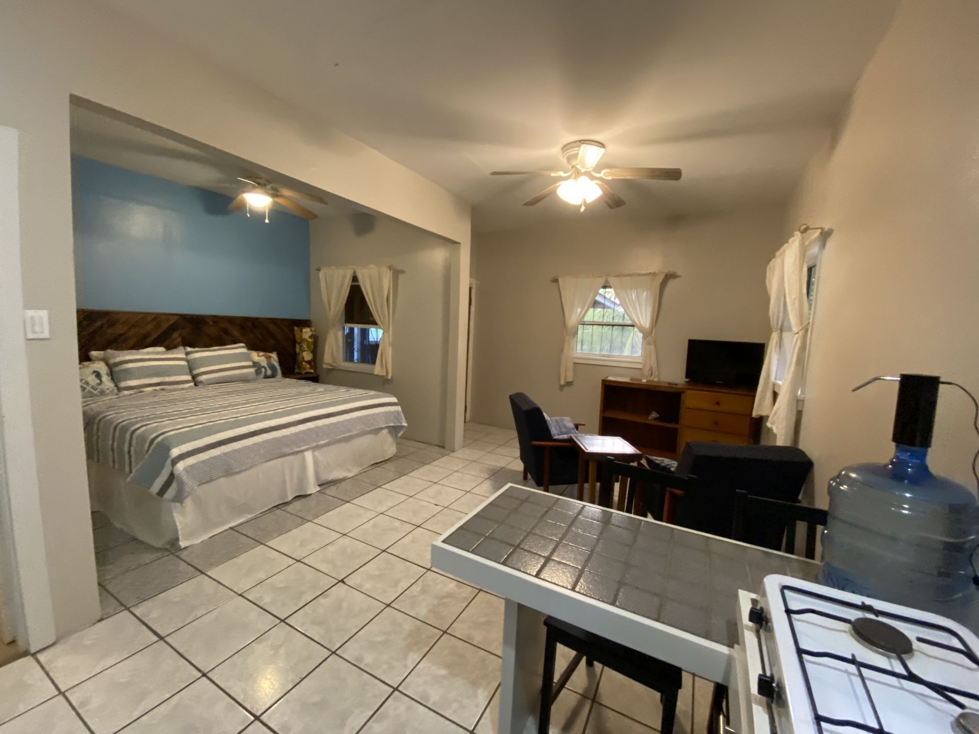 Small studio apartment with bed, small table, and kitchenette. Blue and neutral tones.