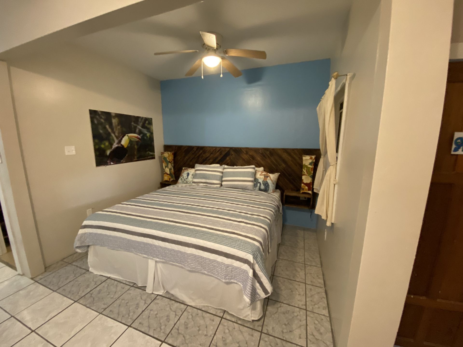 Bedroom with a bed, blue wall, toucan art, and beige tile floor.