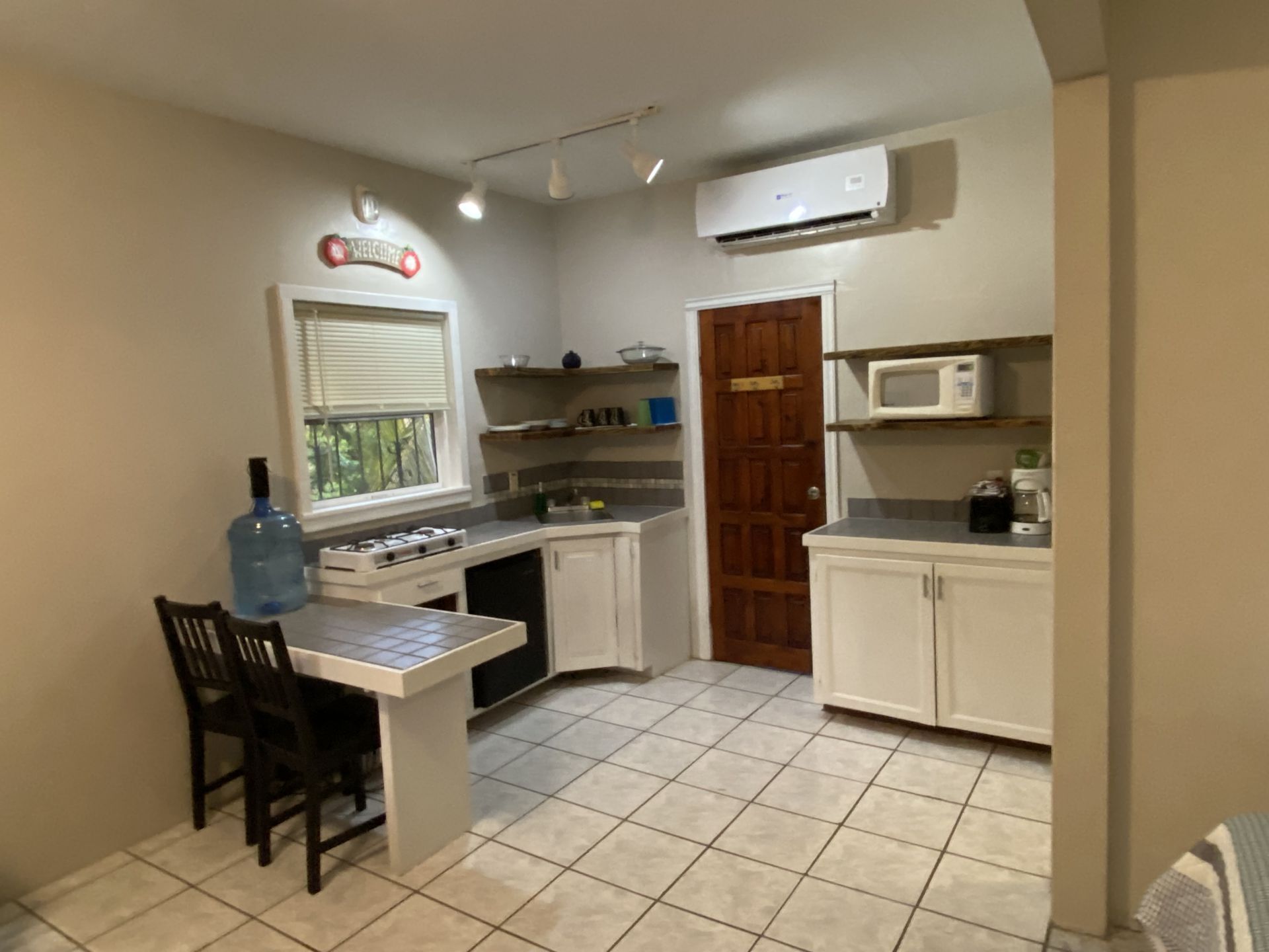 A small kitchen with white cabinets, gray counters, and tile floors; a gas stove, microwave, and window.
