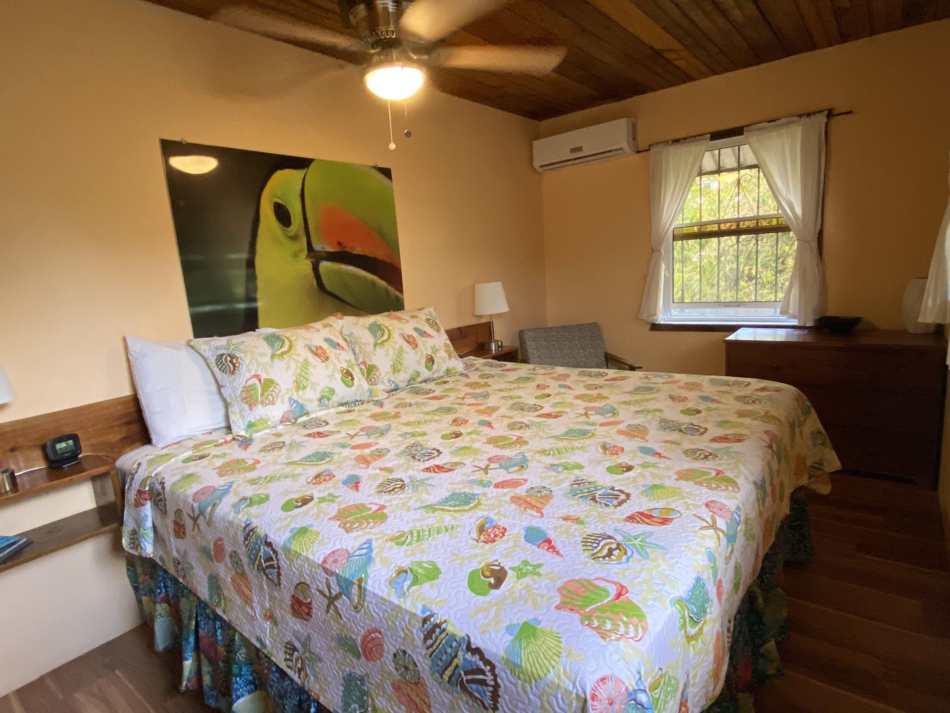 Bedroom with king bed, tropical quilt, toucan artwork, and a window.