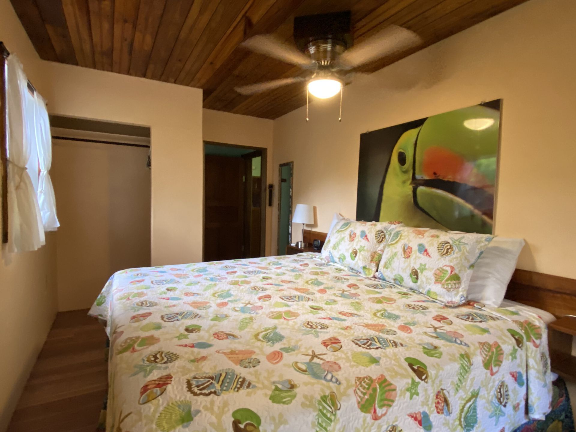Bedroom with king-sized bed, toucan artwork, wood ceiling, closet, and light peach walls.