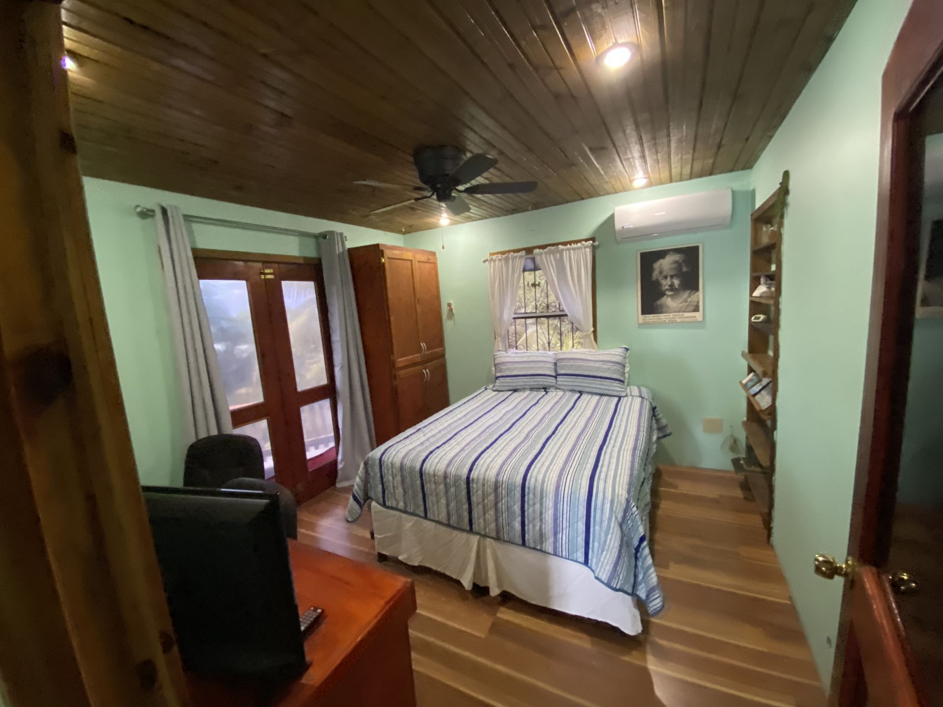 Bedroom with wood ceiling, bed with blue striped cover, light green walls, and a door.