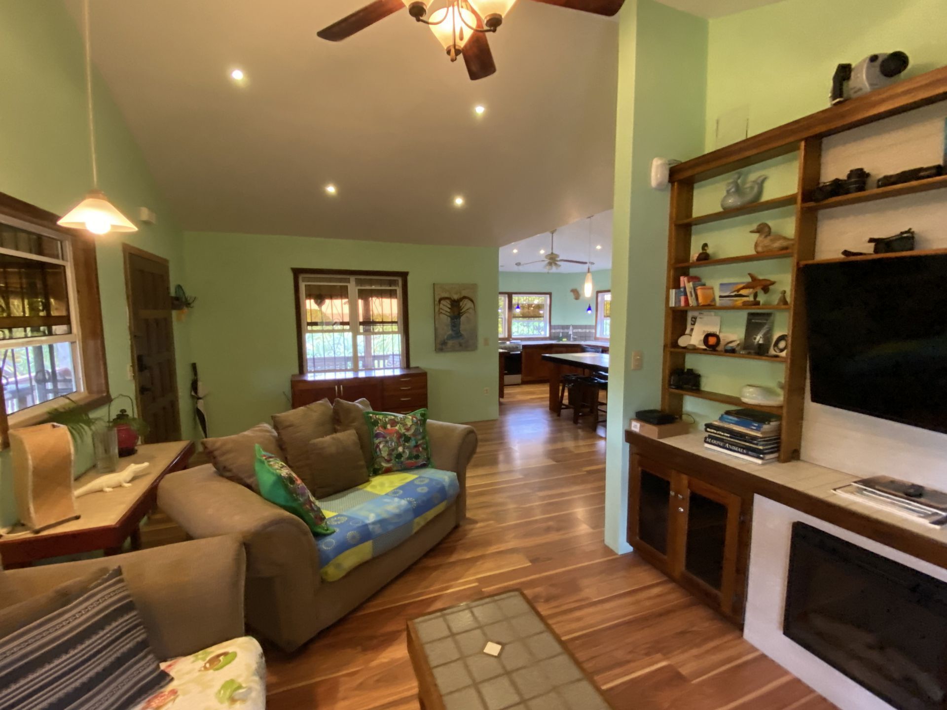 Living room with green walls, wooden floors, sofa, built-in shelving unit, and a view into a kitchen.