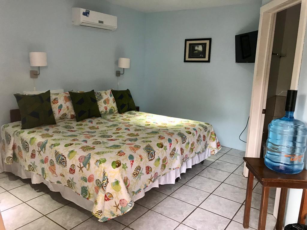 A bedroom with a king-sized bed, blue walls, and white tile flooring. There's a water cooler on a side table.